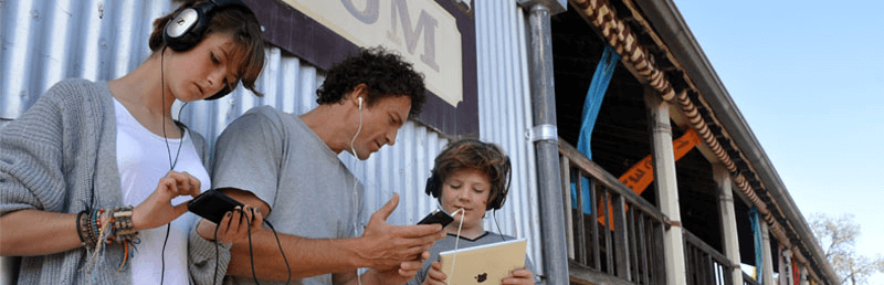 Man and young girl and boy listen to phones and tablet through headphones