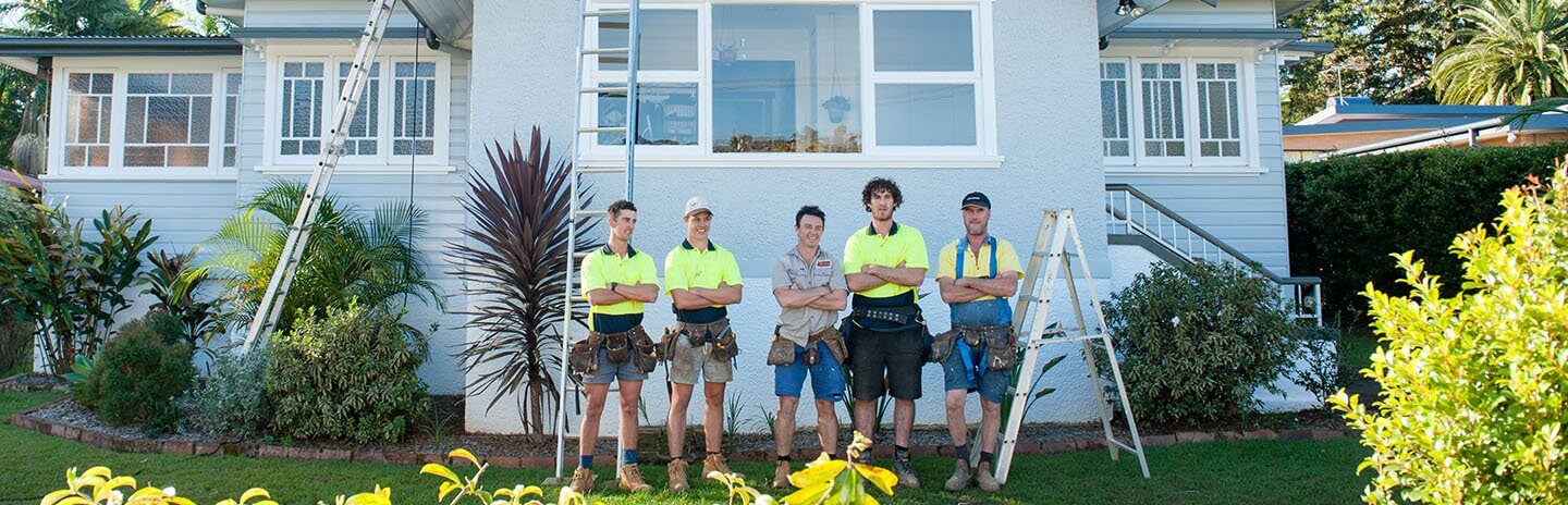 Group of smiling builders and tradies standing outside a house with their arms crossed