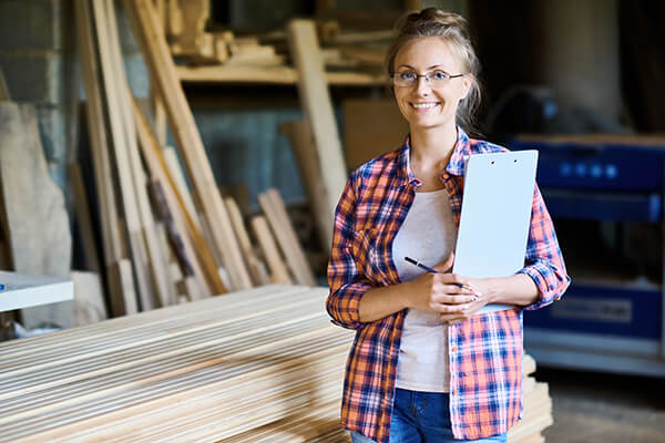 Women dressed in work gear stands with clipboard next to timber in manufacturing area